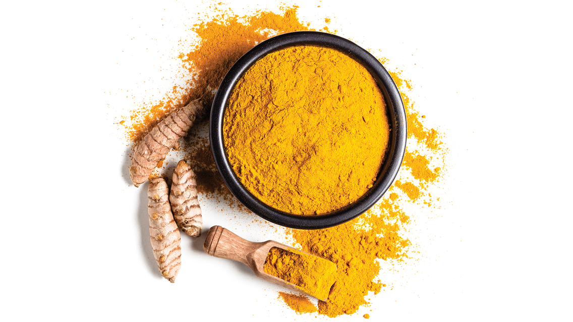 a bowl with powdered turmeric and turmeric roots