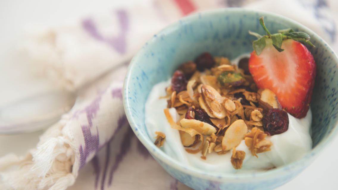 Bowl of yogurt with granola and a strawberry.