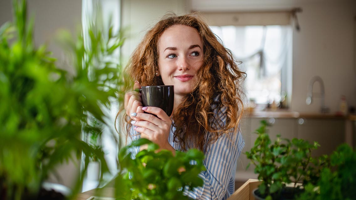 Woman relaxing indoors at home with cup of herbal tea.