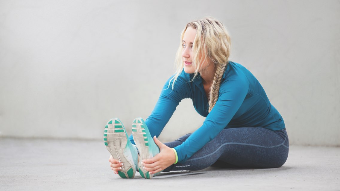A woman sitting and stretching toward her feet.