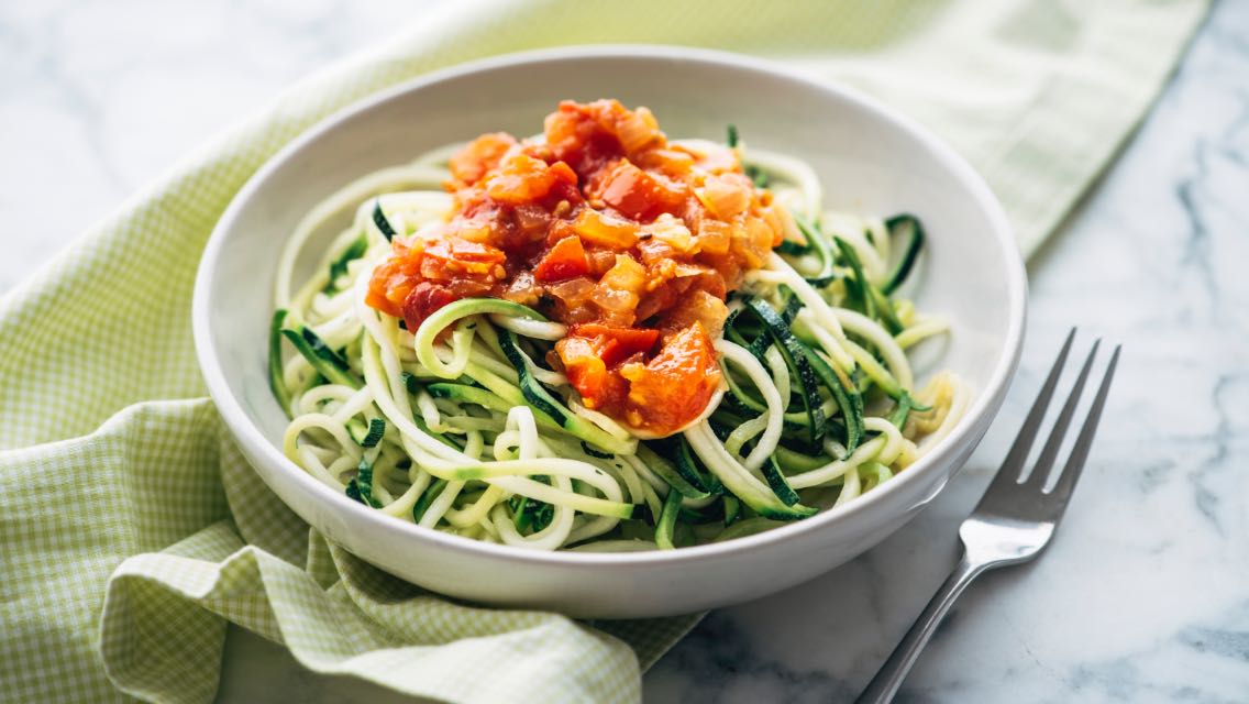 A bowl of zoodles with tomatoes.