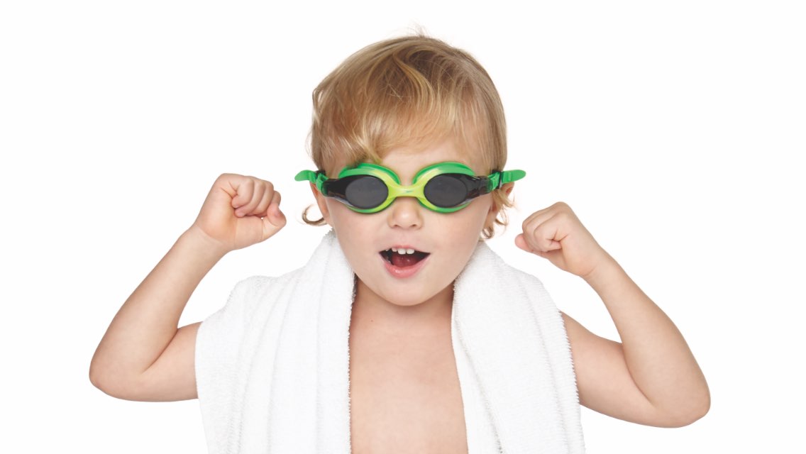Young boy with swimming goggles and towel wrapped around his shoulders.