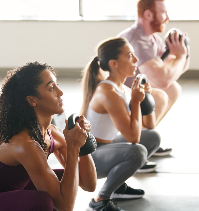 Three people doing a kettlebell squat in a fitness class.