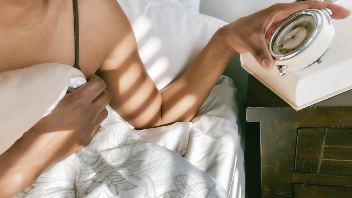 A woman in bed checking her alarm clock.