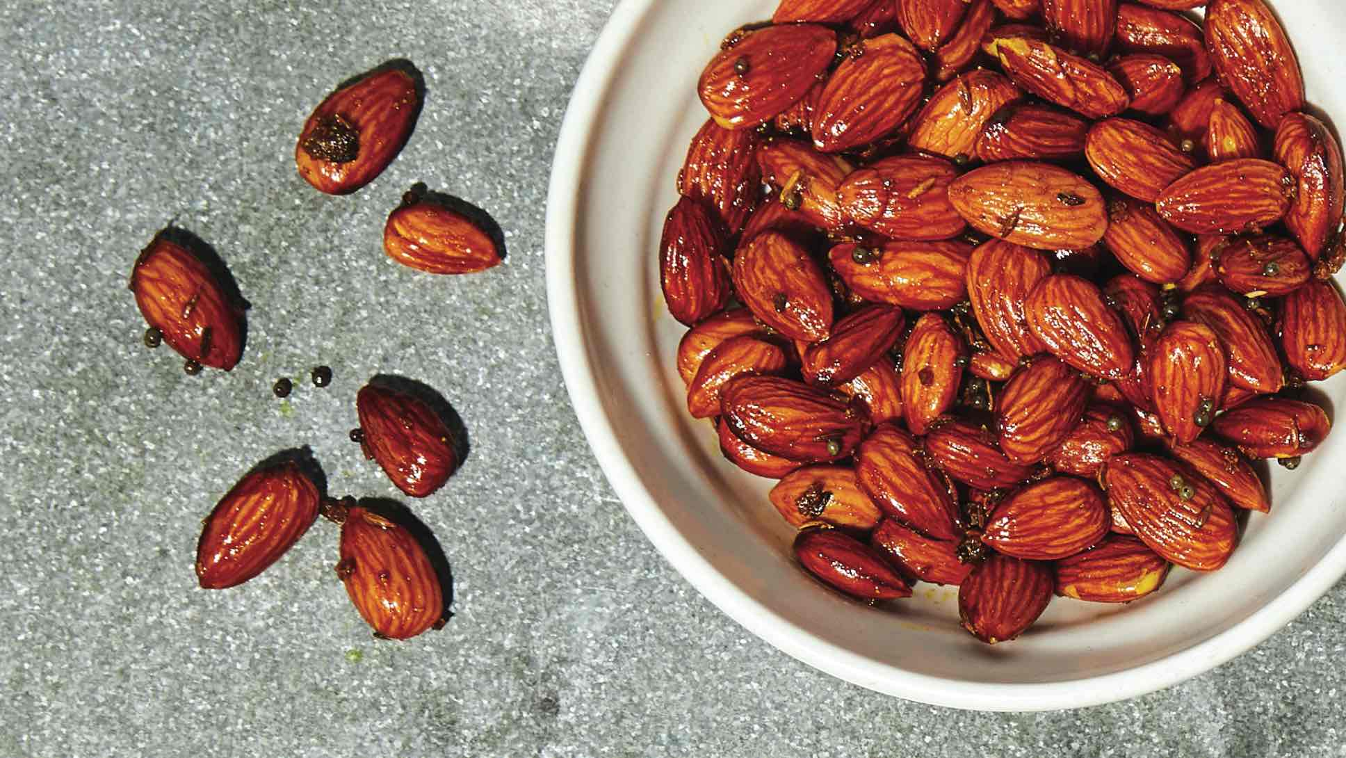 Curry roasted almonds in a bowl and a few on a table.