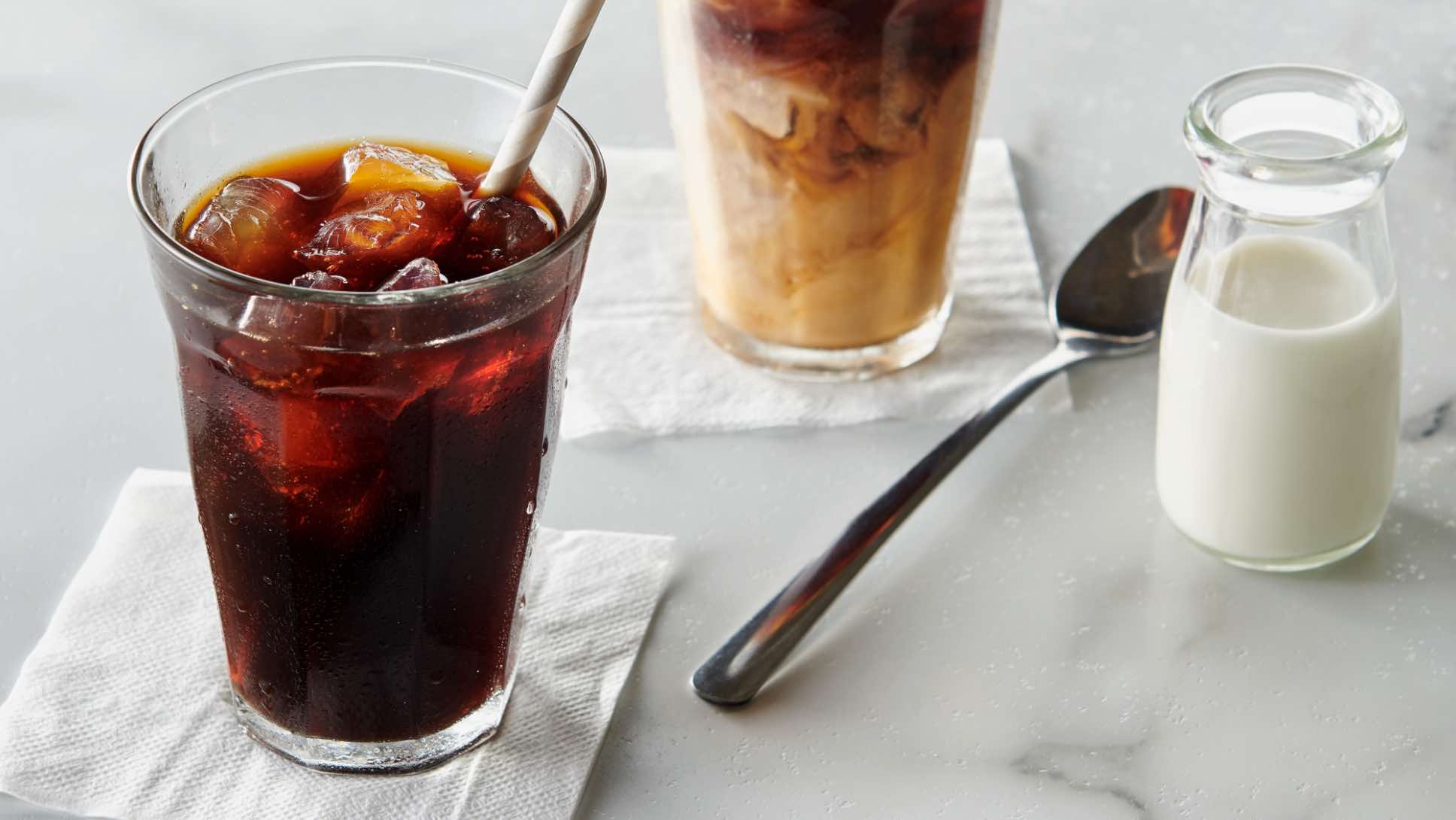 Two glasses of cold brew coffee over ice with a side, small pitcher of coconut milk.