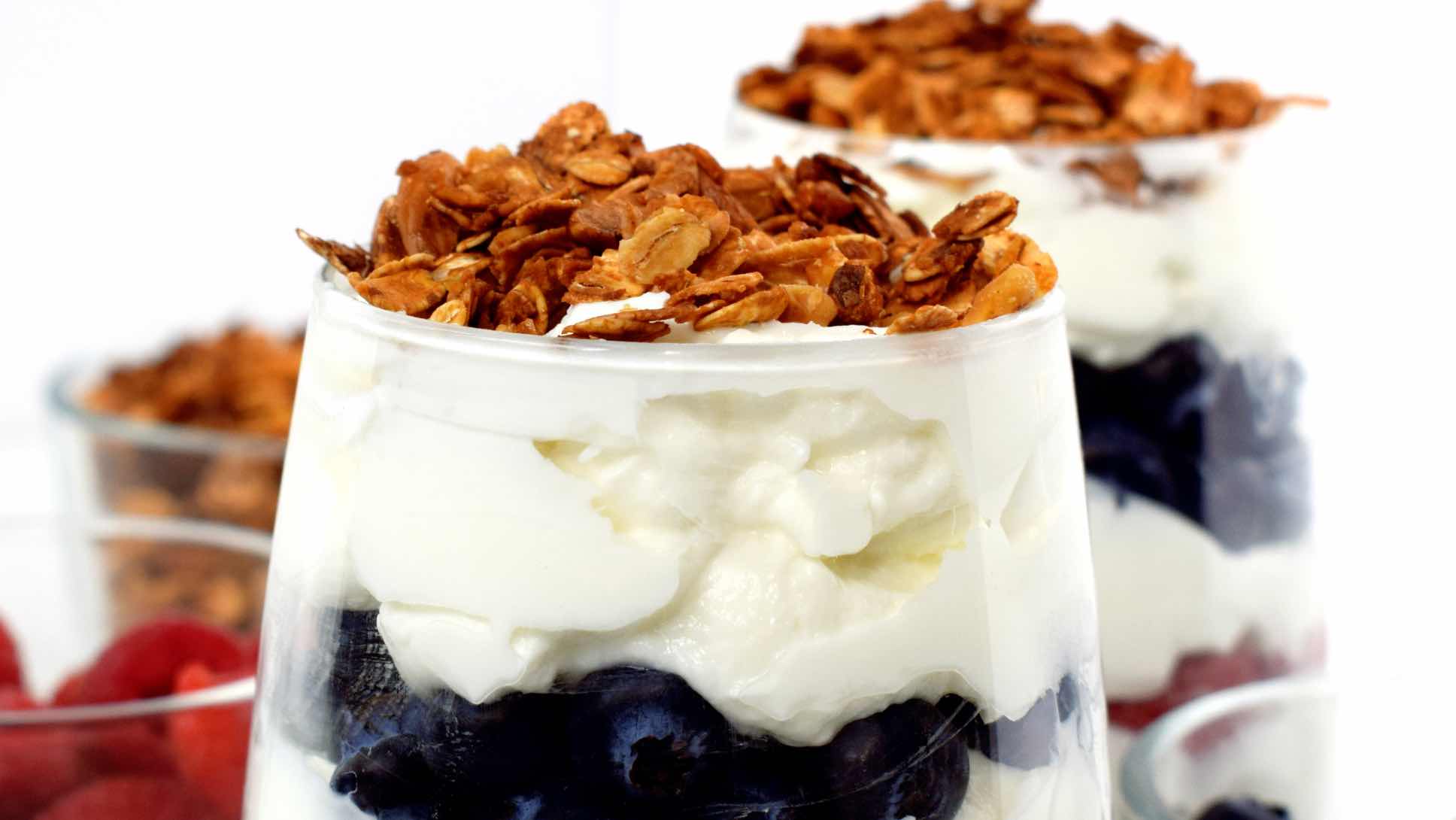 Two cups of a parfait featuring layers of yogurt, red and blue berries, and a topping of granola.