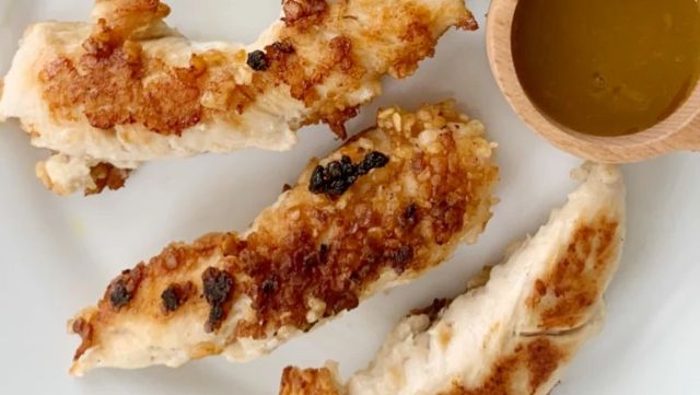 Three fried coconut chicken tenders with a dipping sauce.