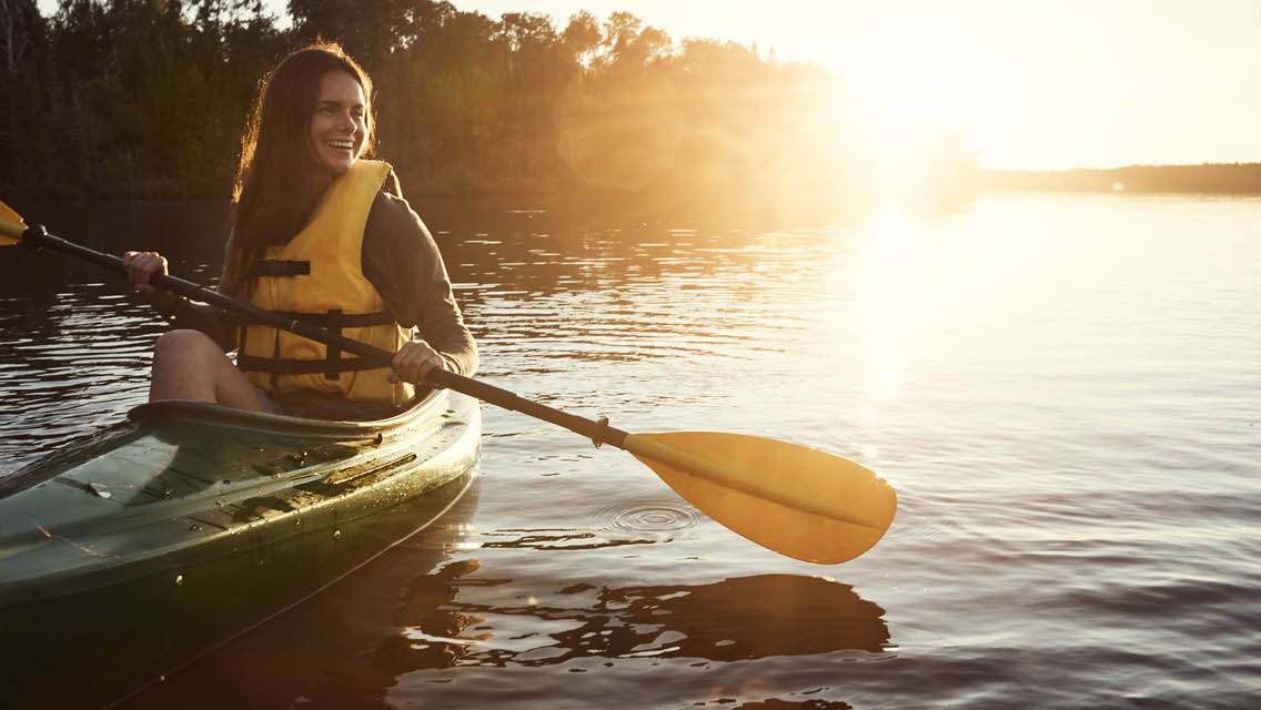 a woman kayaks with the sun setting behind her