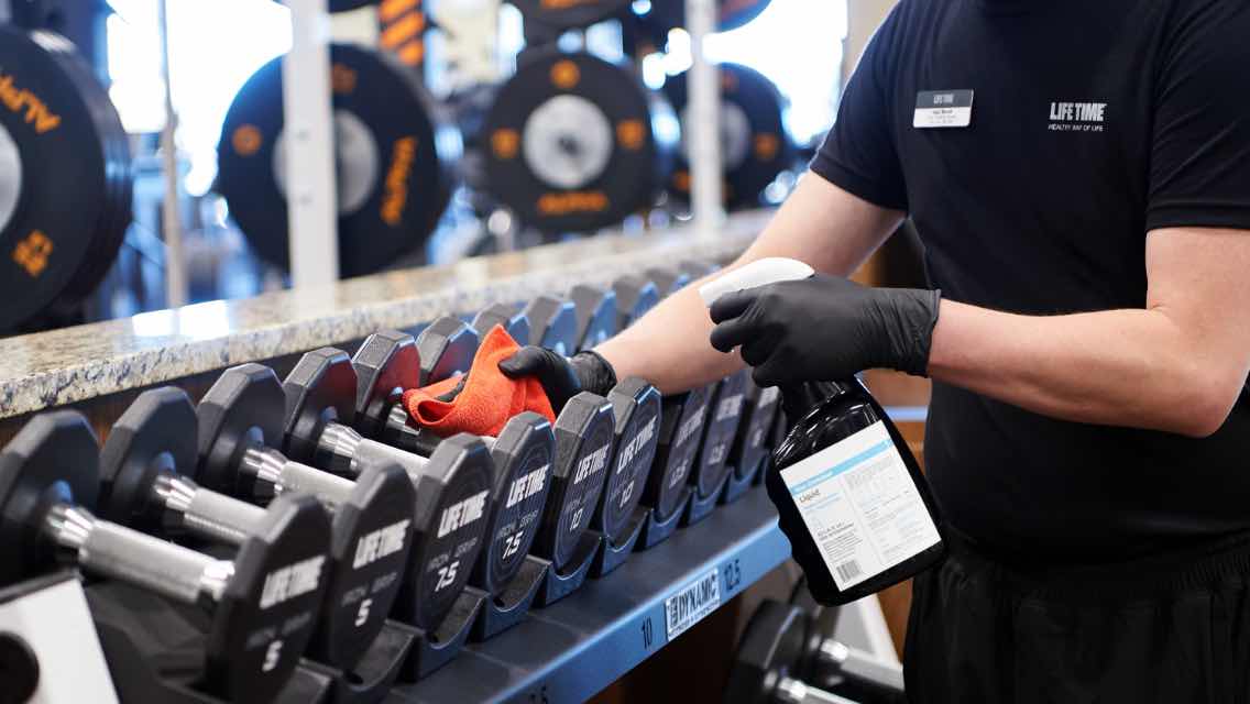 A person cleaning dumbbells in a fitness facility.