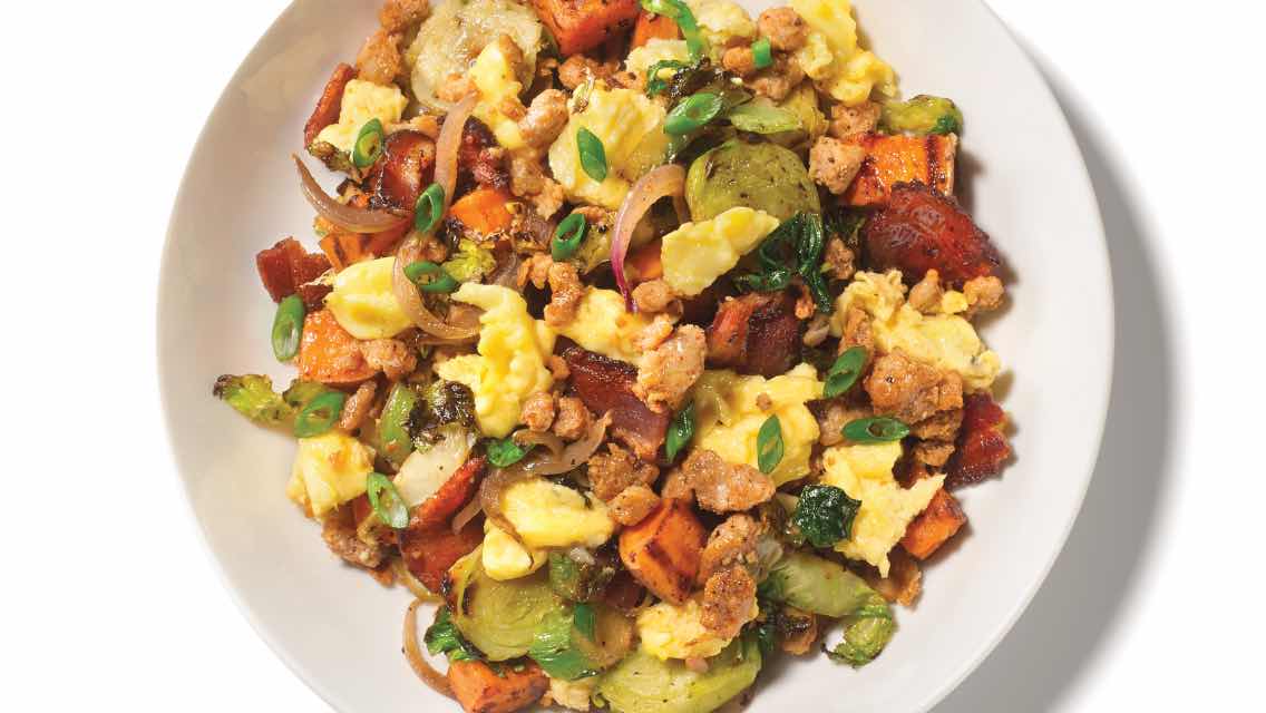A plate of breakfast hash, including eggs, bacon, Brussels sprouts, onion, and more.