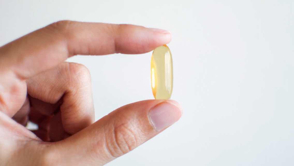 A close up of a hand holding a supplement pill in between two fingers.