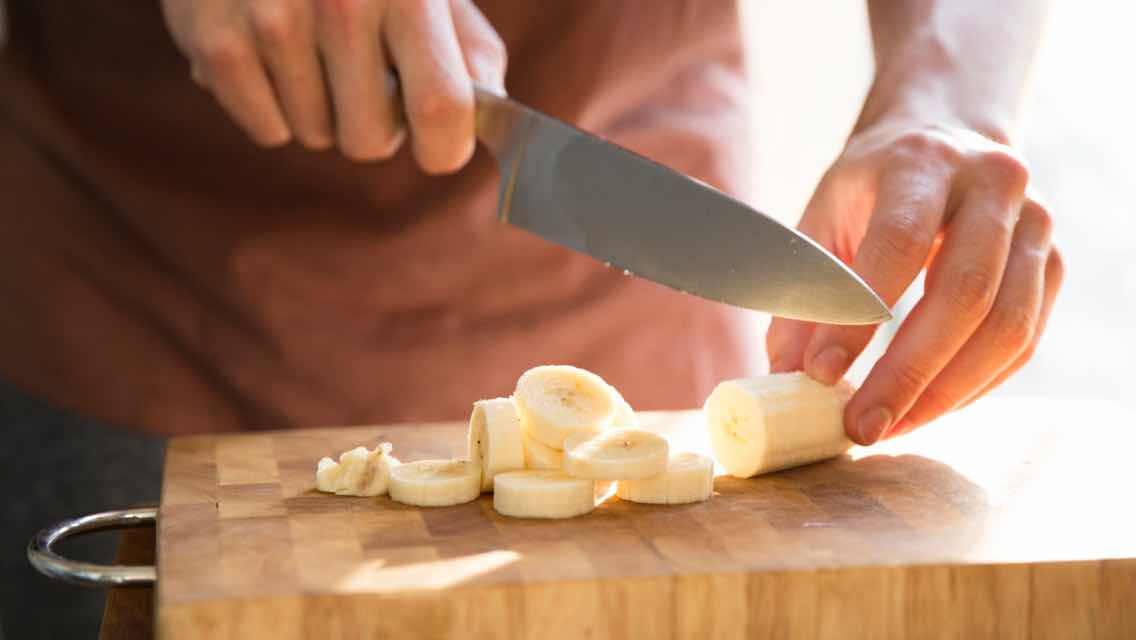 Man cutting a banana into slices on a cutting board.