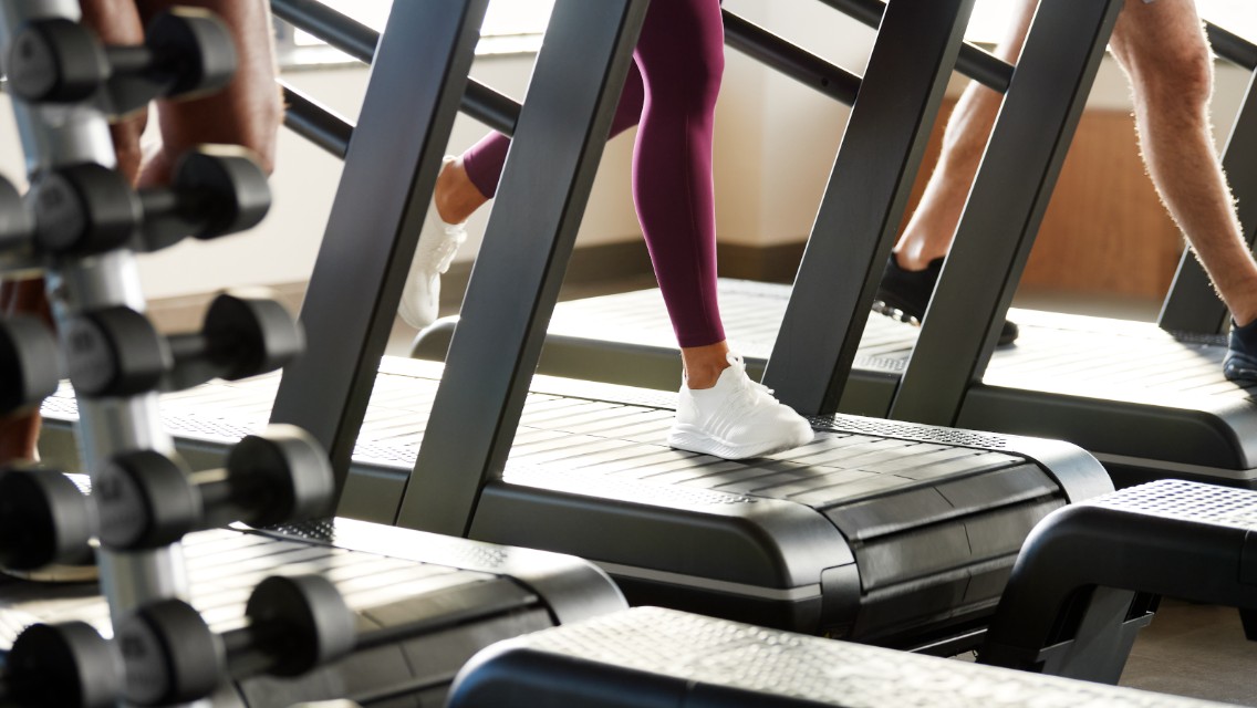 A close up of people's legs running on a treadmill in a health club.