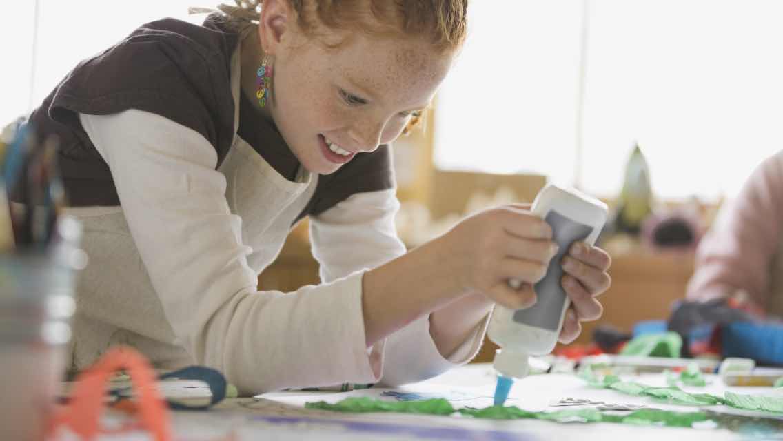 A young girl with a glue bottle doing arts and crafts.