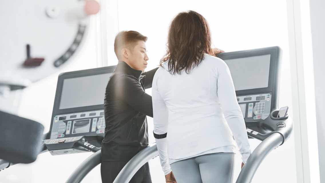 A trainer talking to a client while on a treadmill inside of a fitness facility.