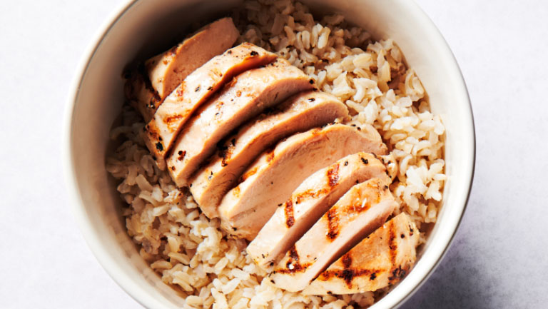 A bowl of brown rice with a chicken breast.