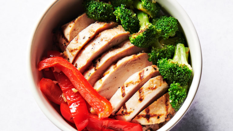 A bowl of brown rice, chicken breast, broccoli, and red pepper.
