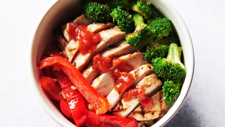 A bowl of brown rice, chicken breast, broccoli, red pepper, and harissa.