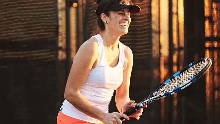 Gigi Skeehan smiling while playing tennis outdoors.