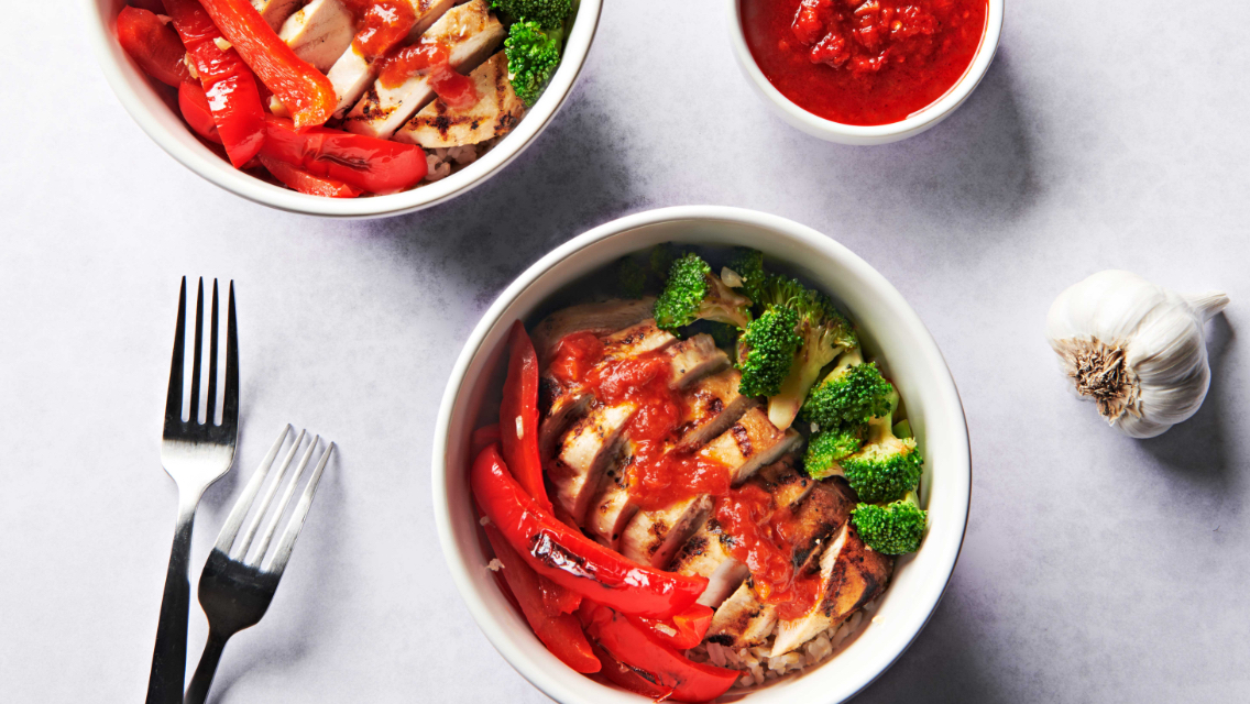 Two LT Bowls, filled with chicken, broccoli, and roasted red pepper, and topped with harissa.