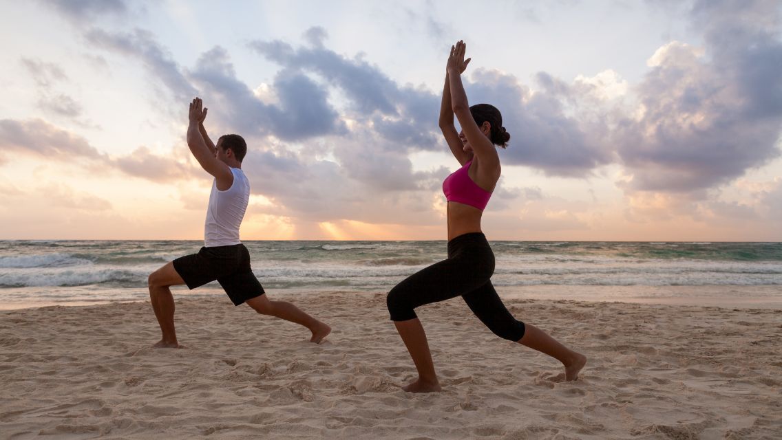 Man and woman doing yoga pose on the beach