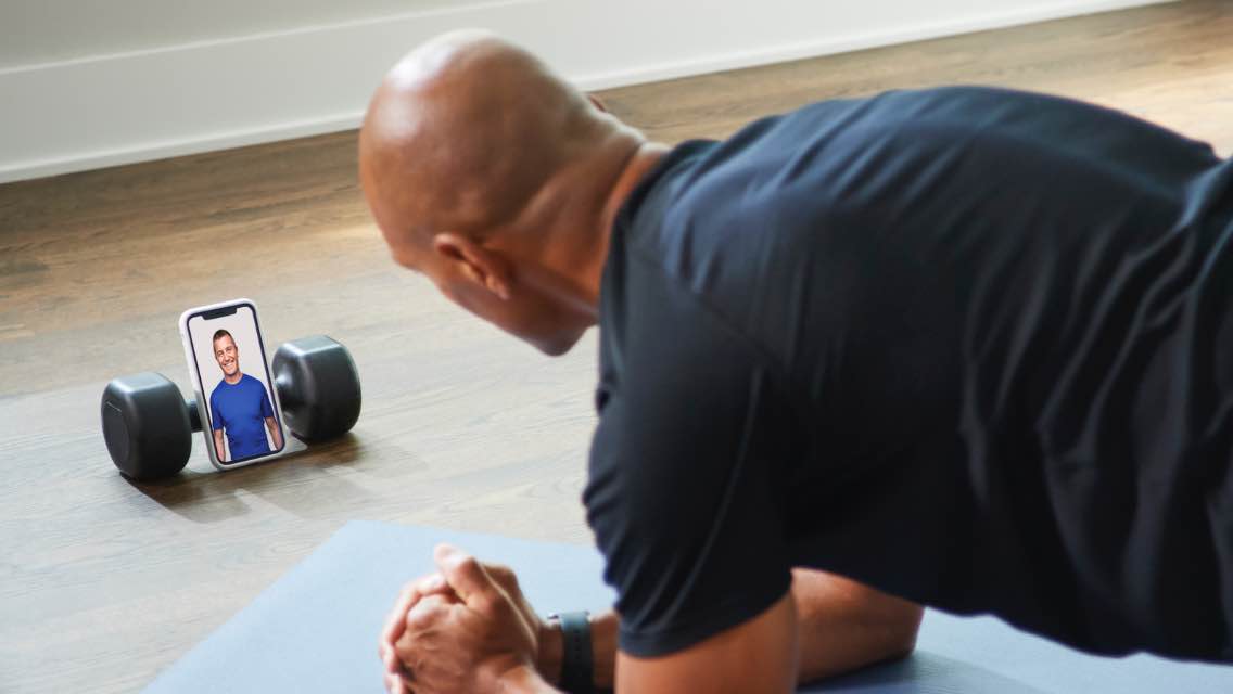 A man in a plank, speaking with someone on his phone propped up against a dumbbell.