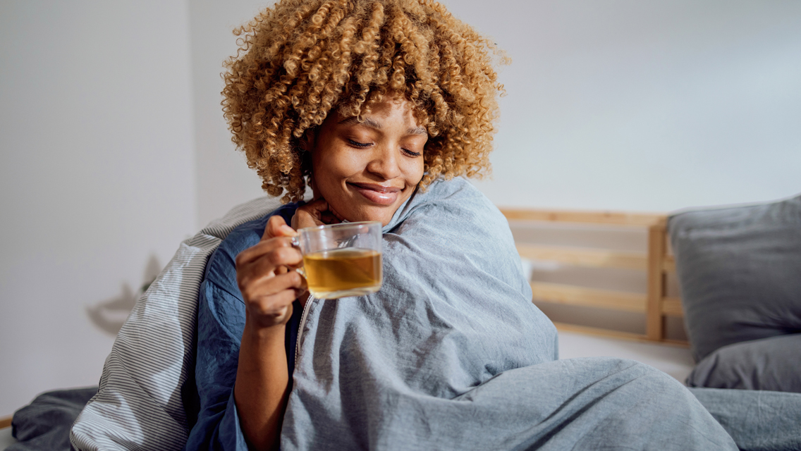 a woman snuggled in a blanket drinking a cup tea