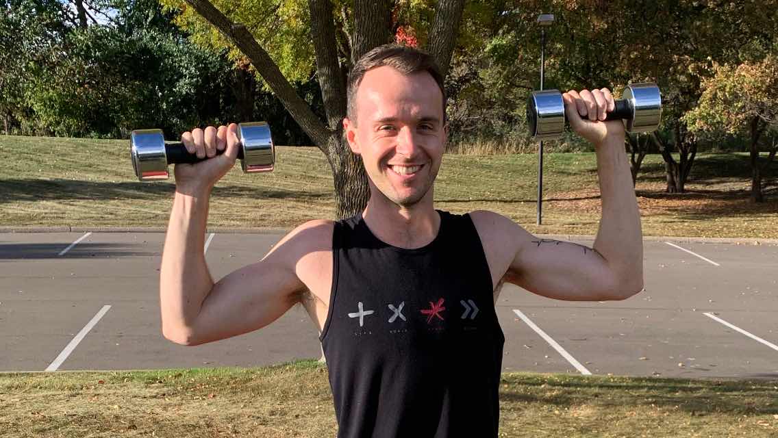 Dan DeBaun, the creator of the workout, flexing while holding two dumbbells.