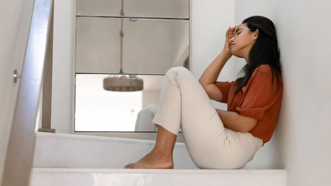 a woman sits at the top of stairs looking stressed and upset