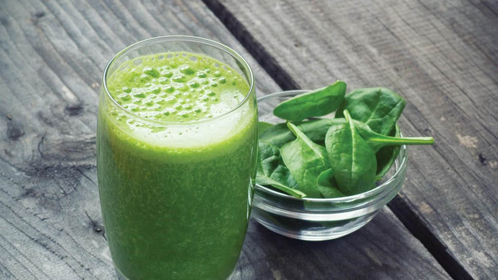 a glass filled with a green smoothie and a bowl of spinach
