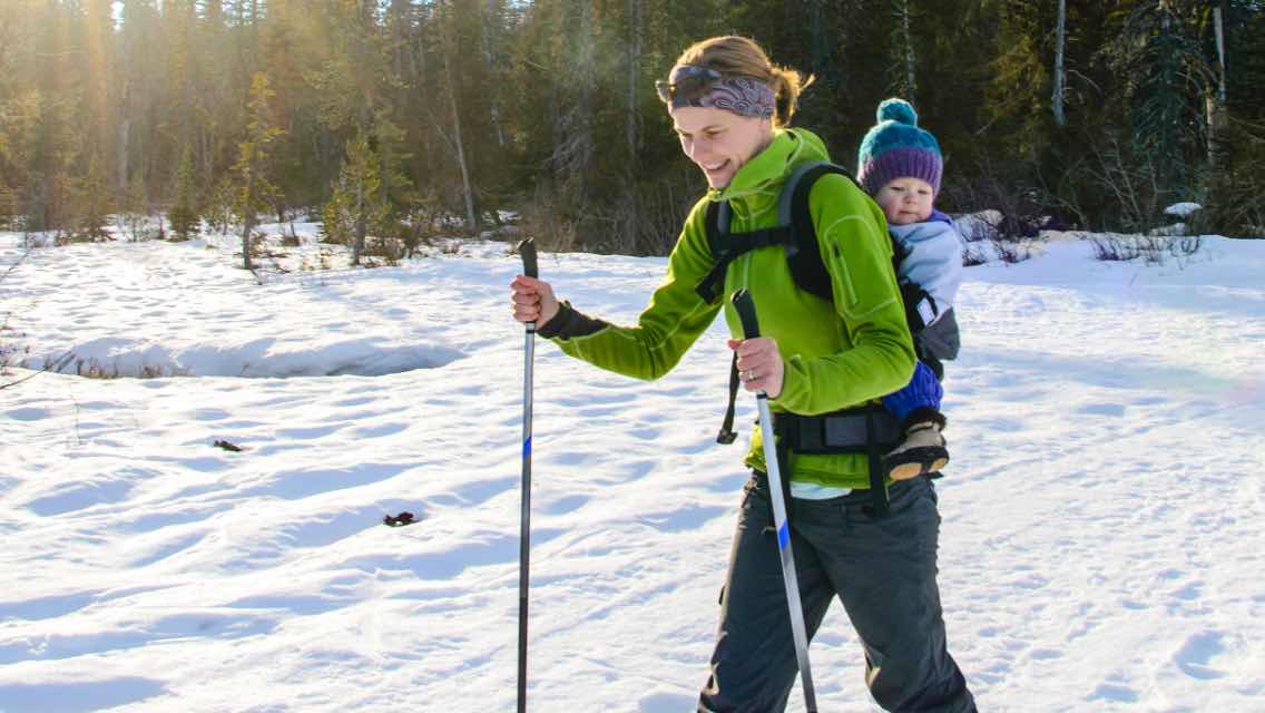 a woman snowshoeing with a toddler on her back