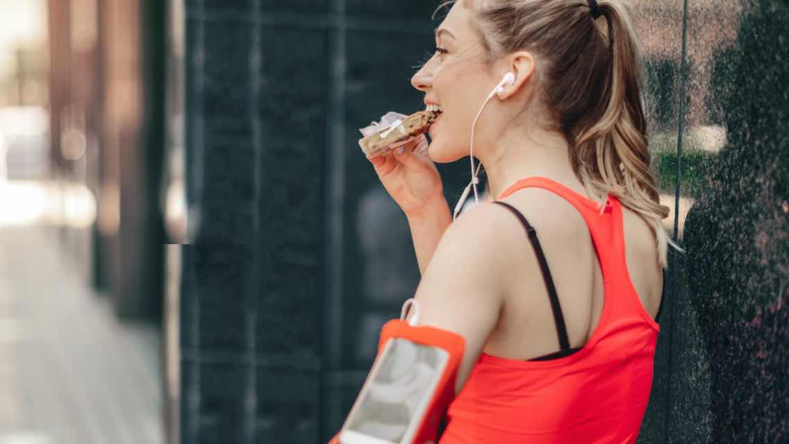 A woman eating a protein bar after exercising.
