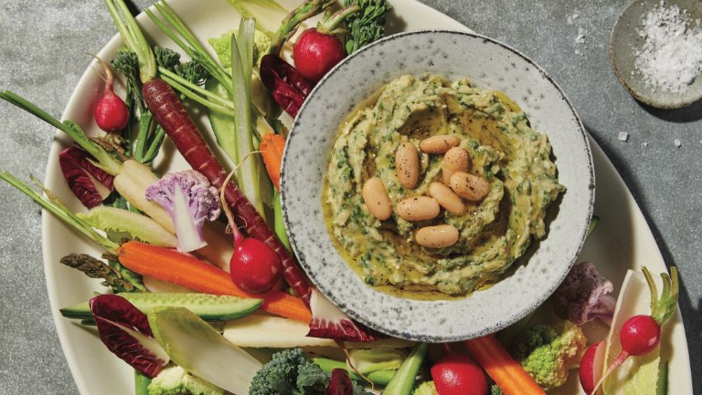 A bowl of creamy spinach and white-bean dip surrounded by raw veggies on a plate.