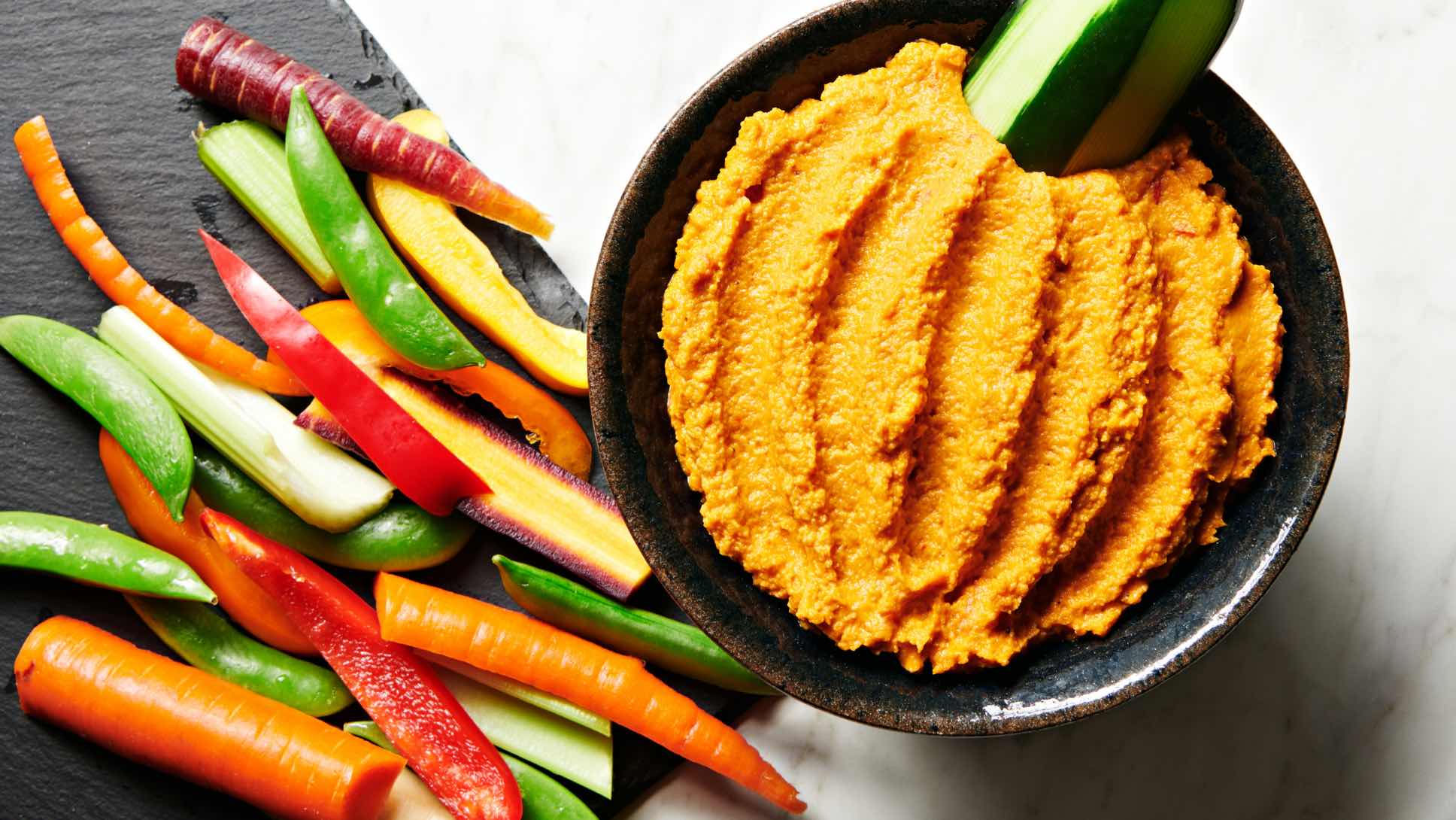 A bowl of Harvest Hummus with raw, sliced veggies on the side.