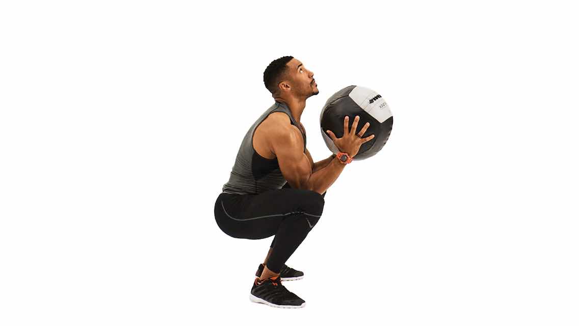 a man sits in a squat position holding a medicine ball