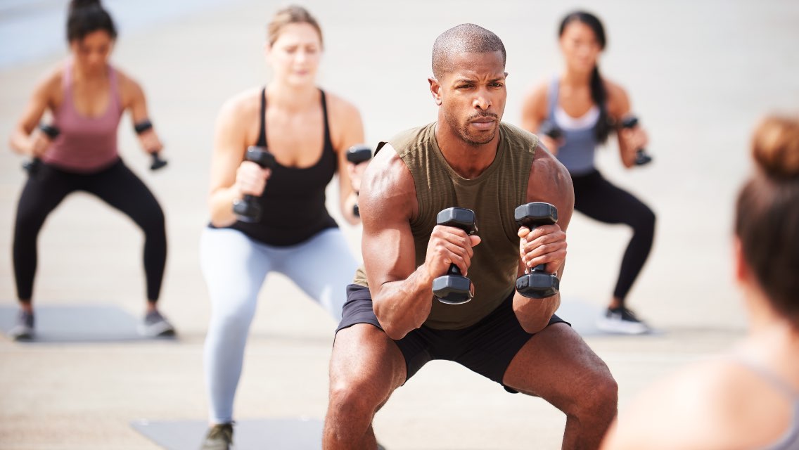 A group of people in a fitness class doing squats with dumbbells.