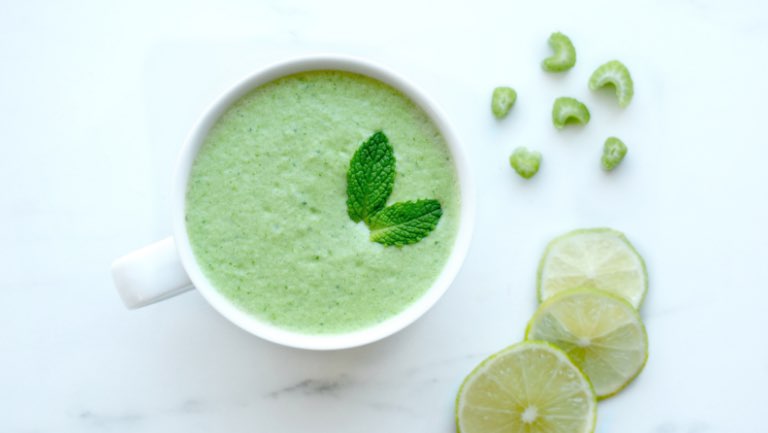 a cup of super greens shakes with lime and celery slices around it