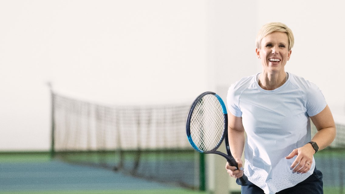 A woman smiling holding a tennis racquet on a tennis court.