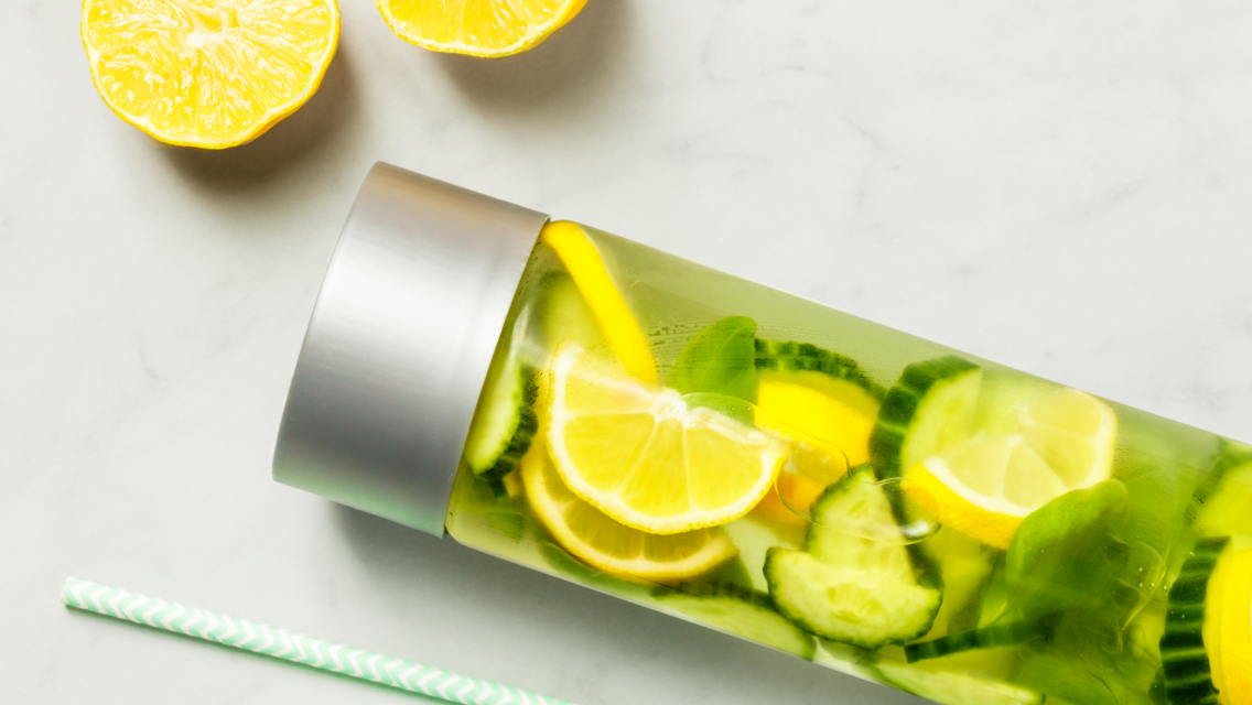a water bottle filled with lemons, limes, ginger, cucumbers and greens