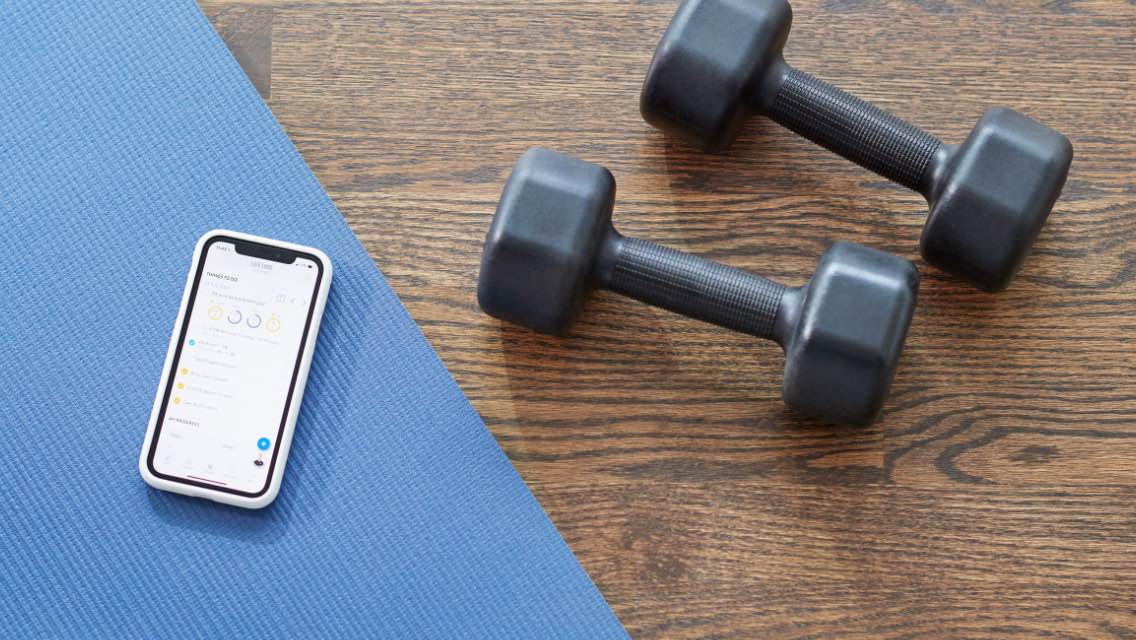 a cell phone sits on a yoga mat with dumb bells nearby