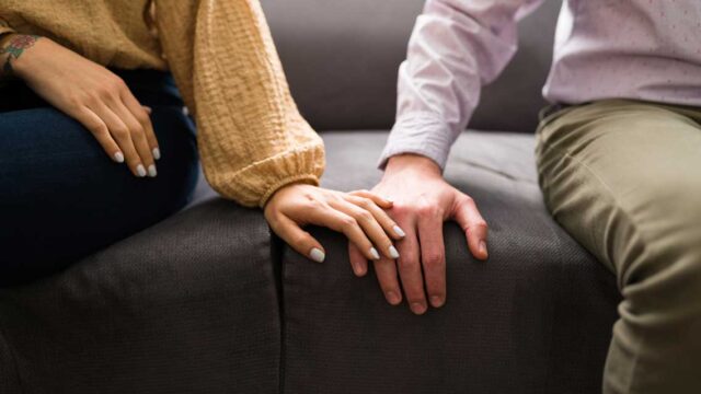Two people's hands touch on a couch.