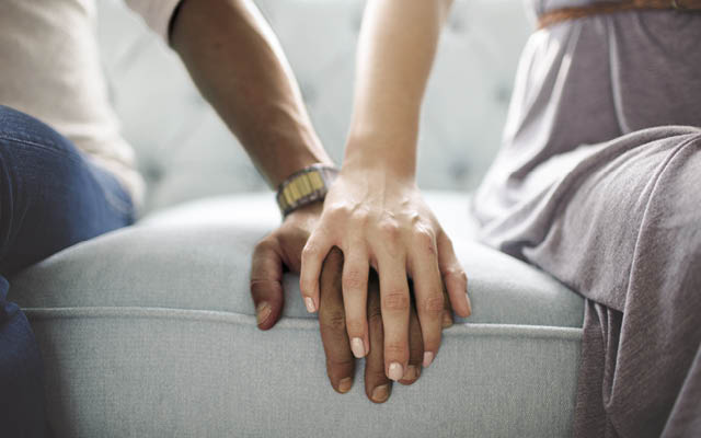 Two people's hands touch on a couch.