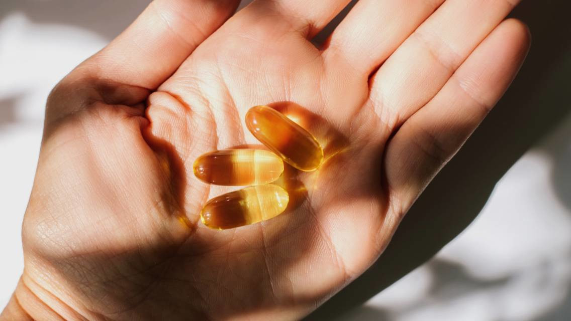 A palm holding three capsules of a supplement.