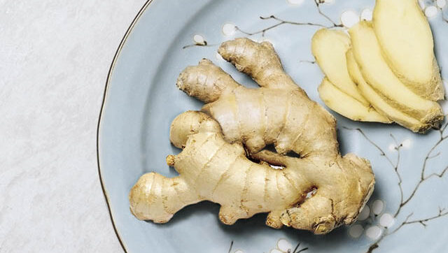 A hand of ginger and some slices on a plate