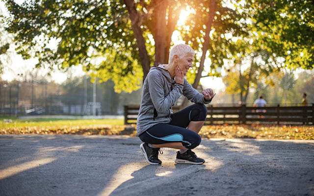 An older woman who is jogging checks her heart rate.