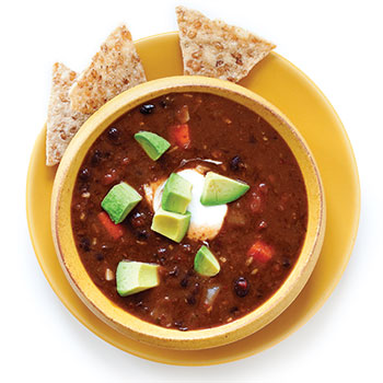 A bowl of black-bean soup with chips and avocado