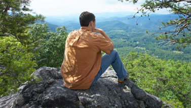 man sitting on rock overlooking a valley