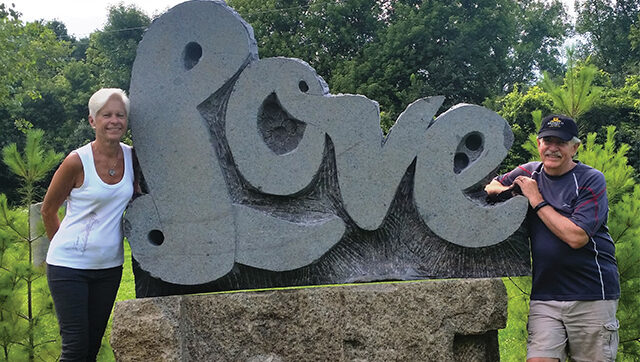two people standing in front of a love sculpture