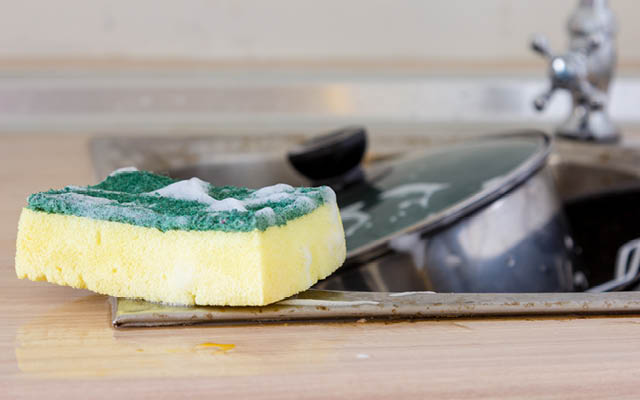 A kitchen sponge next to sink and dirty dishes